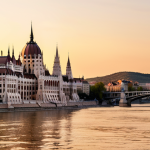 **Prompt:** Picturesque view of the Danube River in Budapest, Hungary, with the Hungarian Parliament Building in the background. Golden hour lighting. Elegant apartment building with balconies overlooking the water. Focus on luxury and lifestyle appeal.